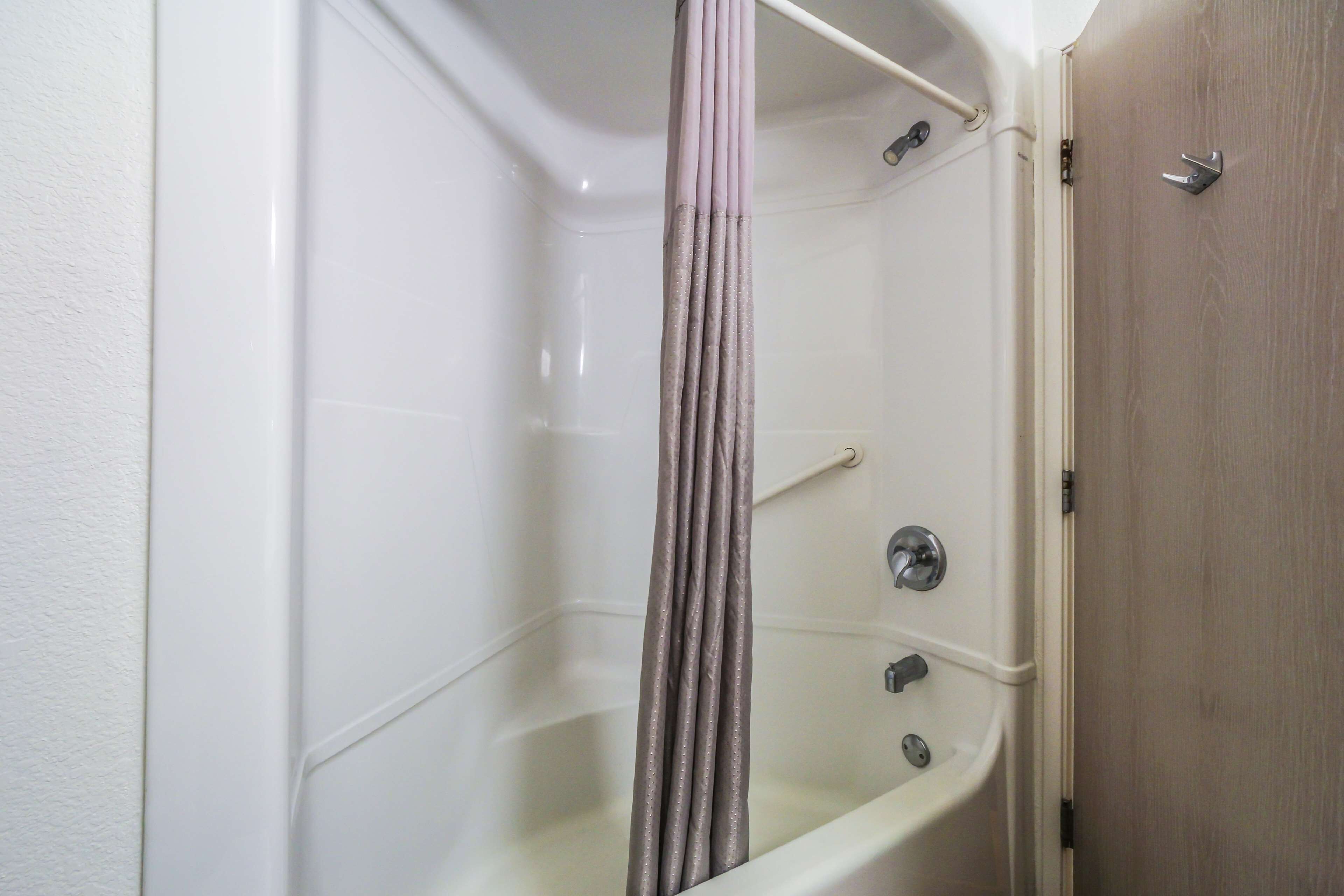 A corner of a bathroom with a bathtub, a shower curtain, and a wooden door.