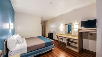 Een kleine hotelkamer met een bed, een bureau, een stoel, een televisie en een kledingkast.