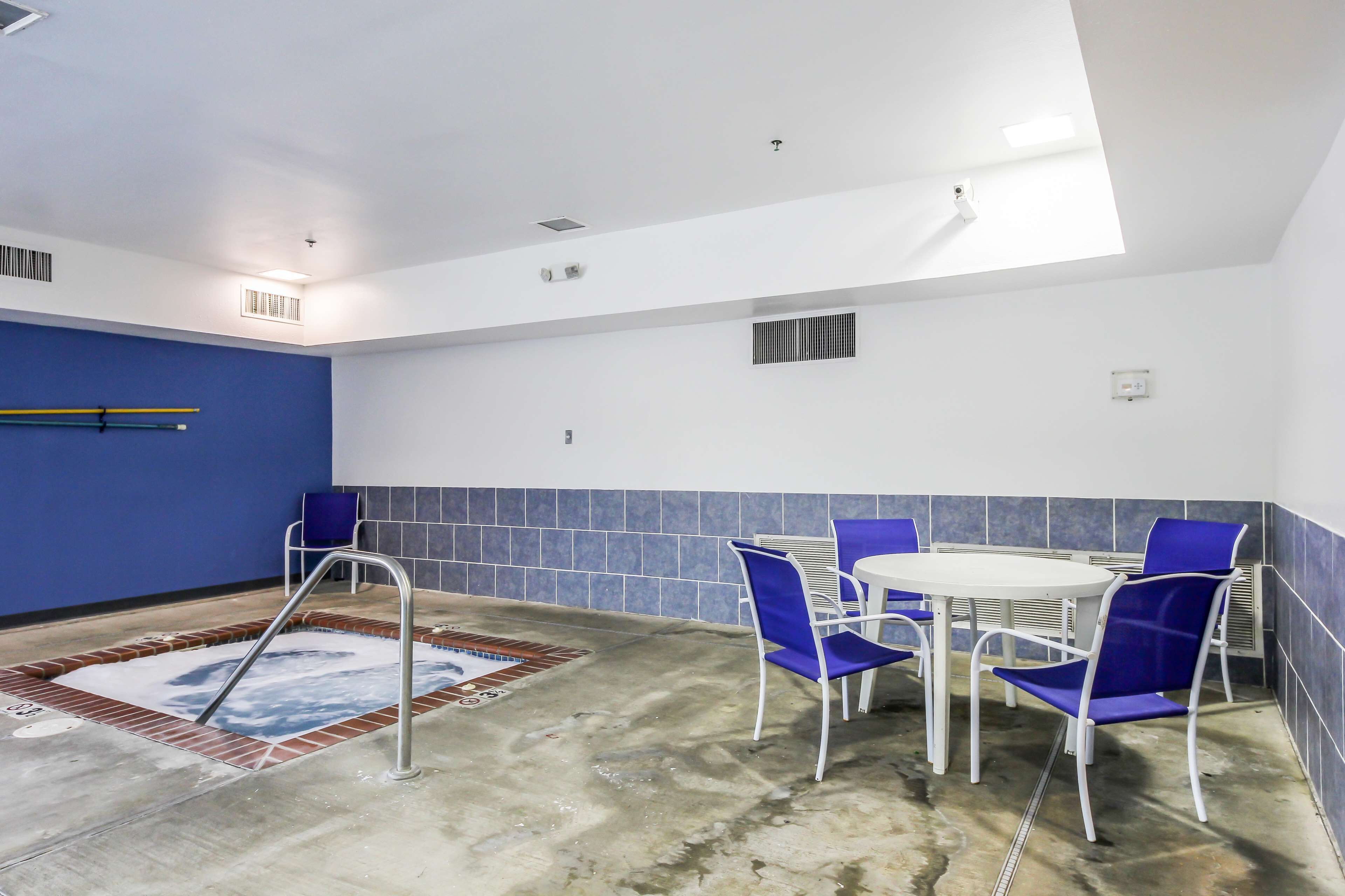 A pool area with a hot tub, blue chairs, and a white table.