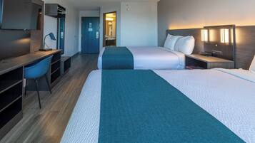 A hotel room with two beds, a desk, a chair, a TV, and a bathroom visible through an open door.