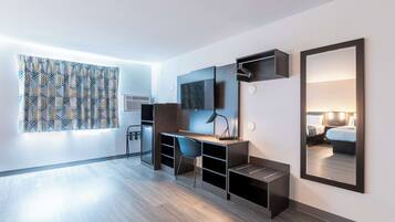 A modern hotel room with a wooden desk, a chair, a flat-screen TV, a mirror, and a bed with a headboard.