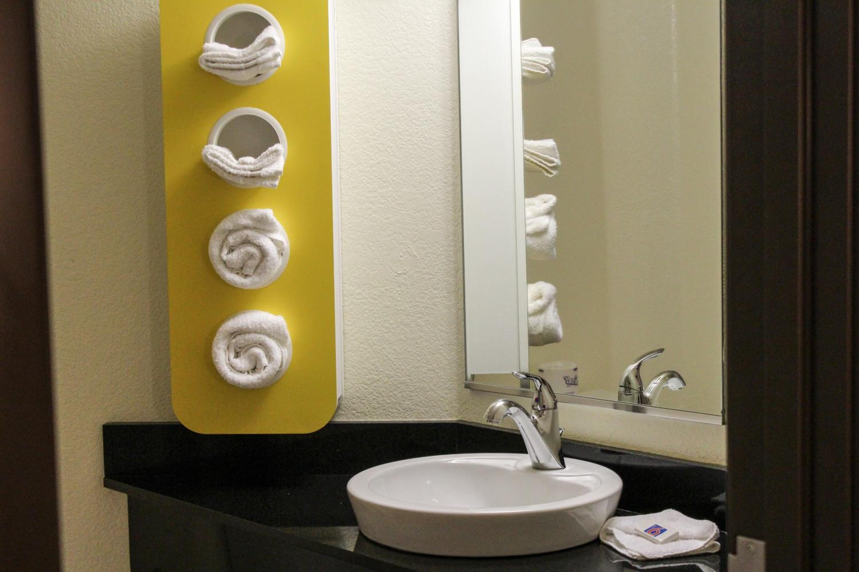 Ein Badezimmer mit einem weißen Waschbecken, einem Spiegel und vier weißen Handtüchern an einer gelben Wand.