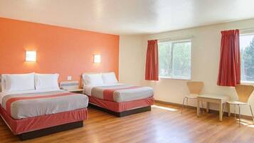 Quarto de hotel com duas camas, uma mesa pequena, duas cadeiras e uma janela com cortinas.