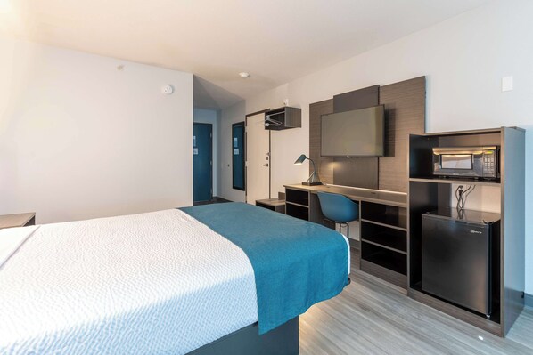Una habitación de hotel moderna con cama, escritorio, silla, televisor y microondas integrado.