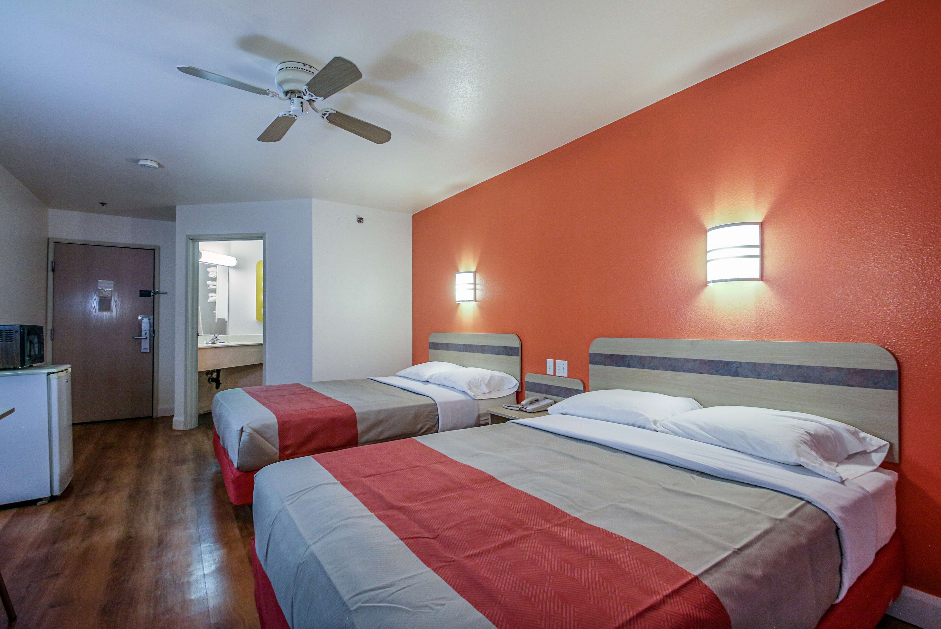 A hotel room with two beds, a ceiling fan, and a kitchenette.