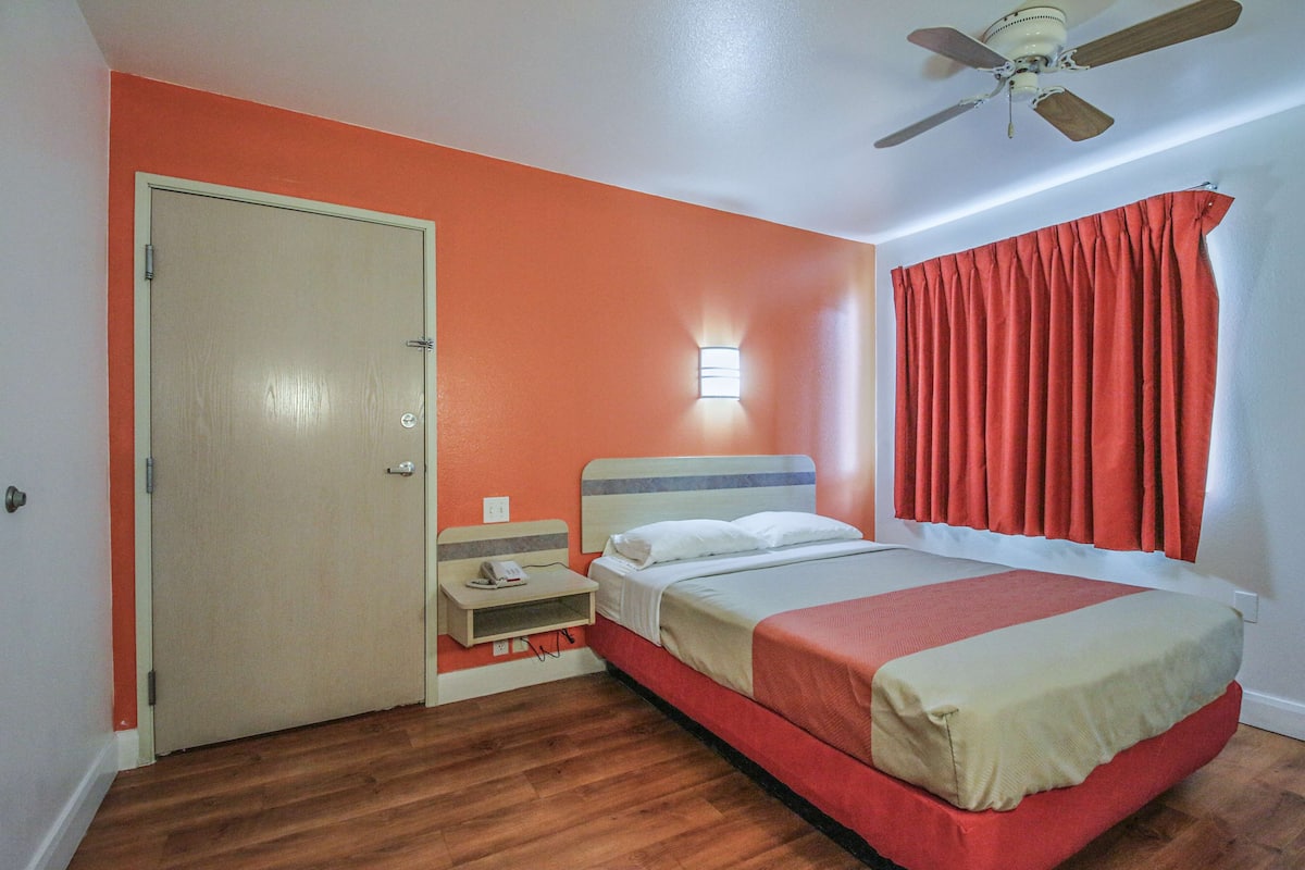 Une chambre à coucher avec un lit, une table de chevet, un ventilateur de plafond et une fenêtre avec des rideaux.