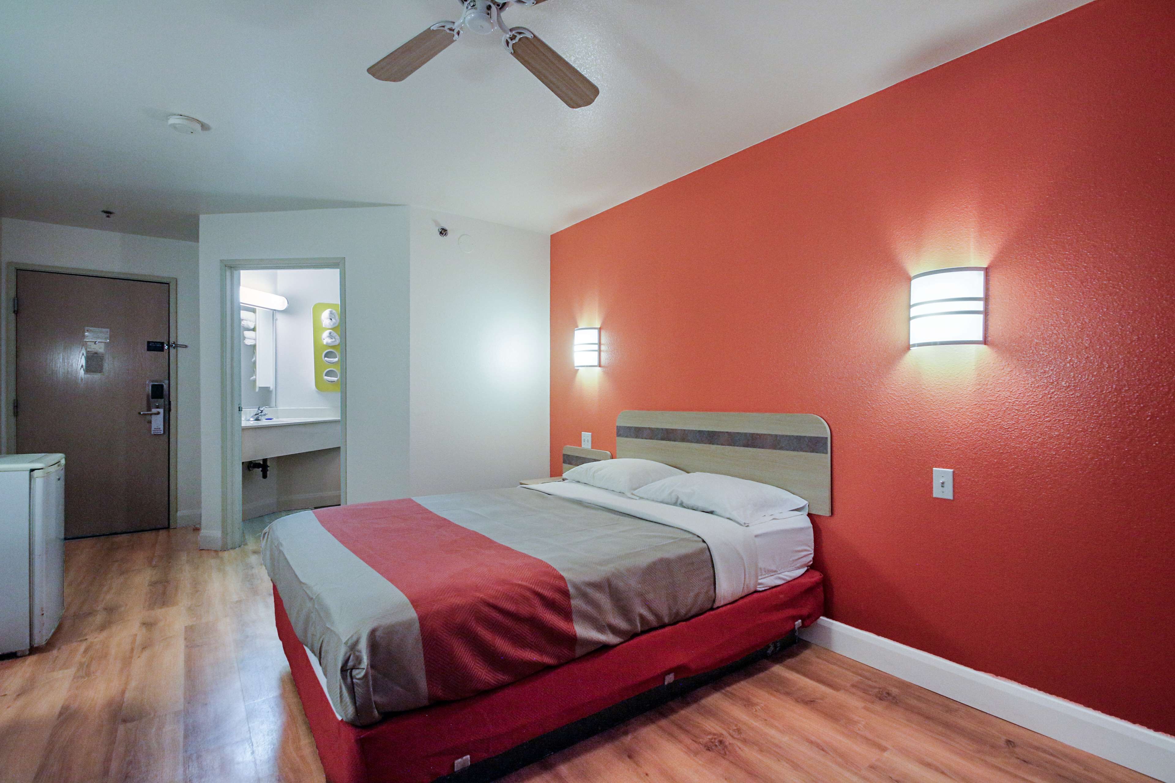 Un dormitorio con cama, piso de madera, ventilador de techo y dos lámparas fijadas a la pared.