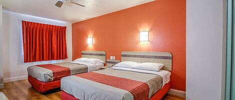 Habitación de hotel con dos camas, un ventilador de techo y dos luces fijadas a la pared.