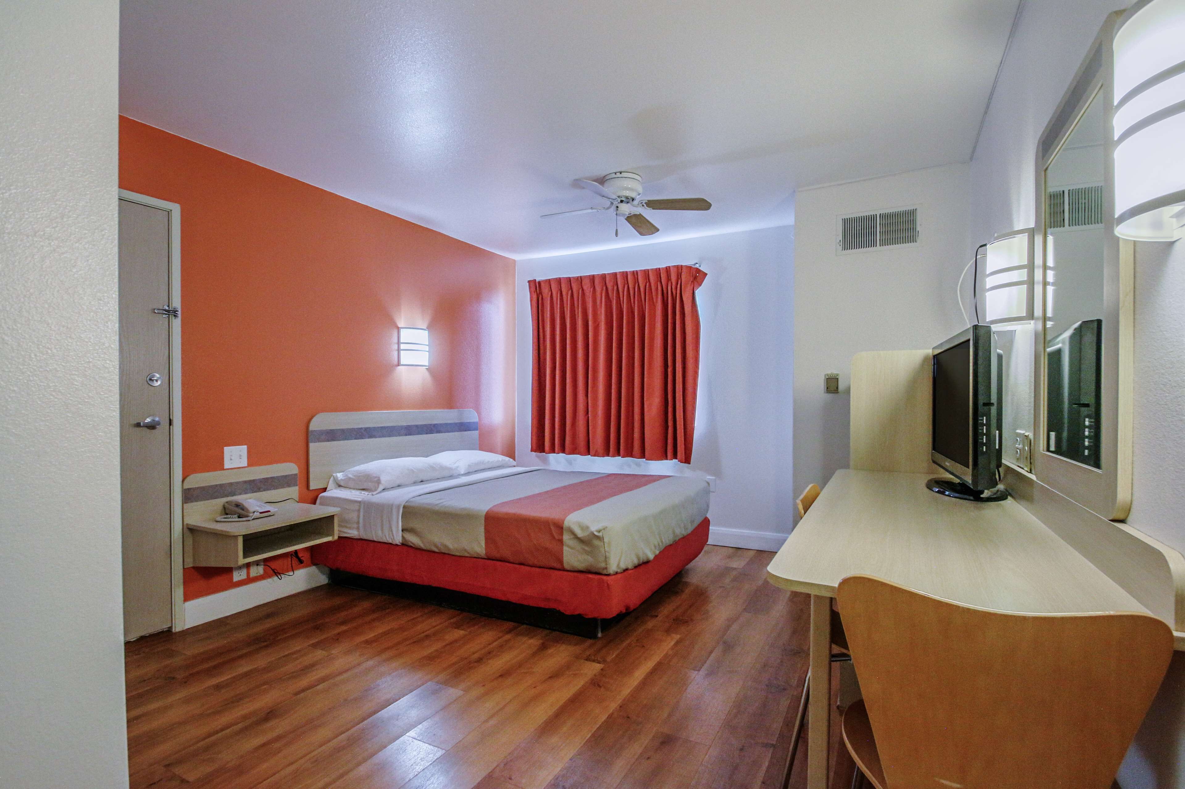 A hotel room with a bed, a desk, a television, and a ceiling fan.