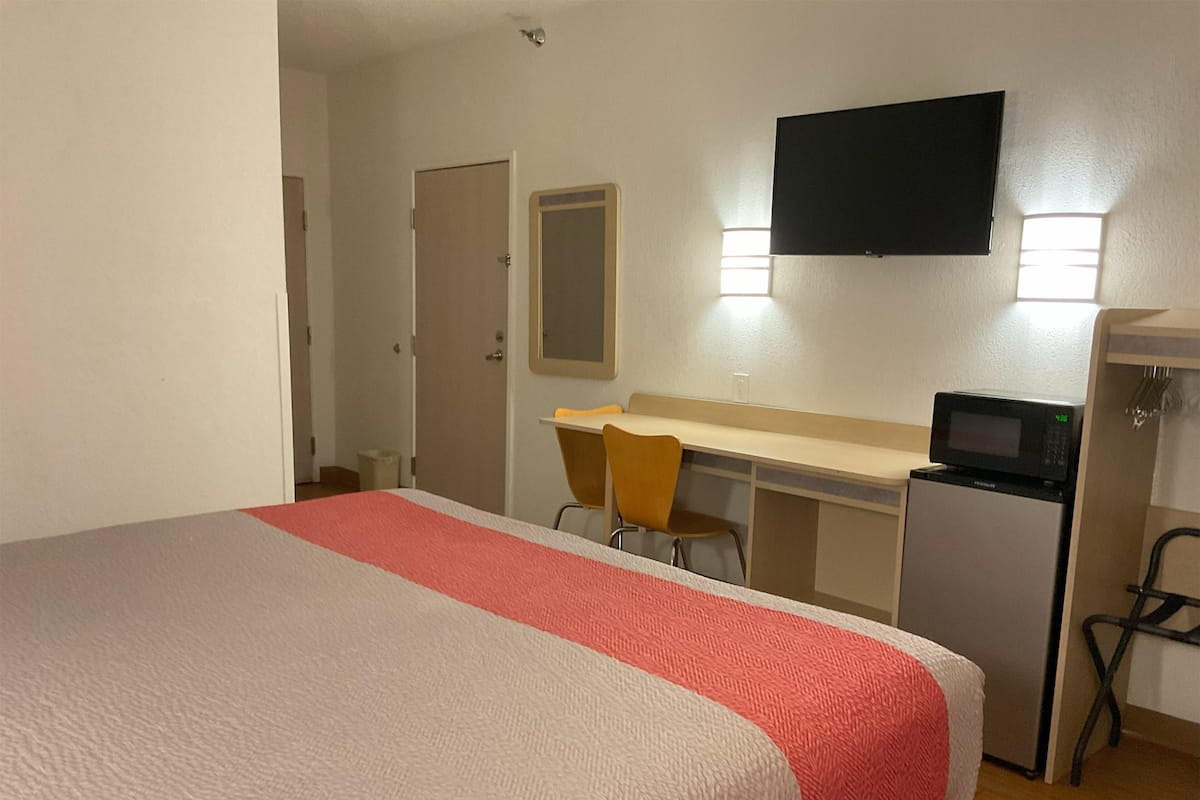 A hotel room with a bed, a desk, a chair, a television, and a microwave.