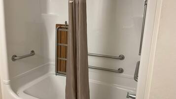A bathroom with a bathtub, a shower area, and a wooden shelf.