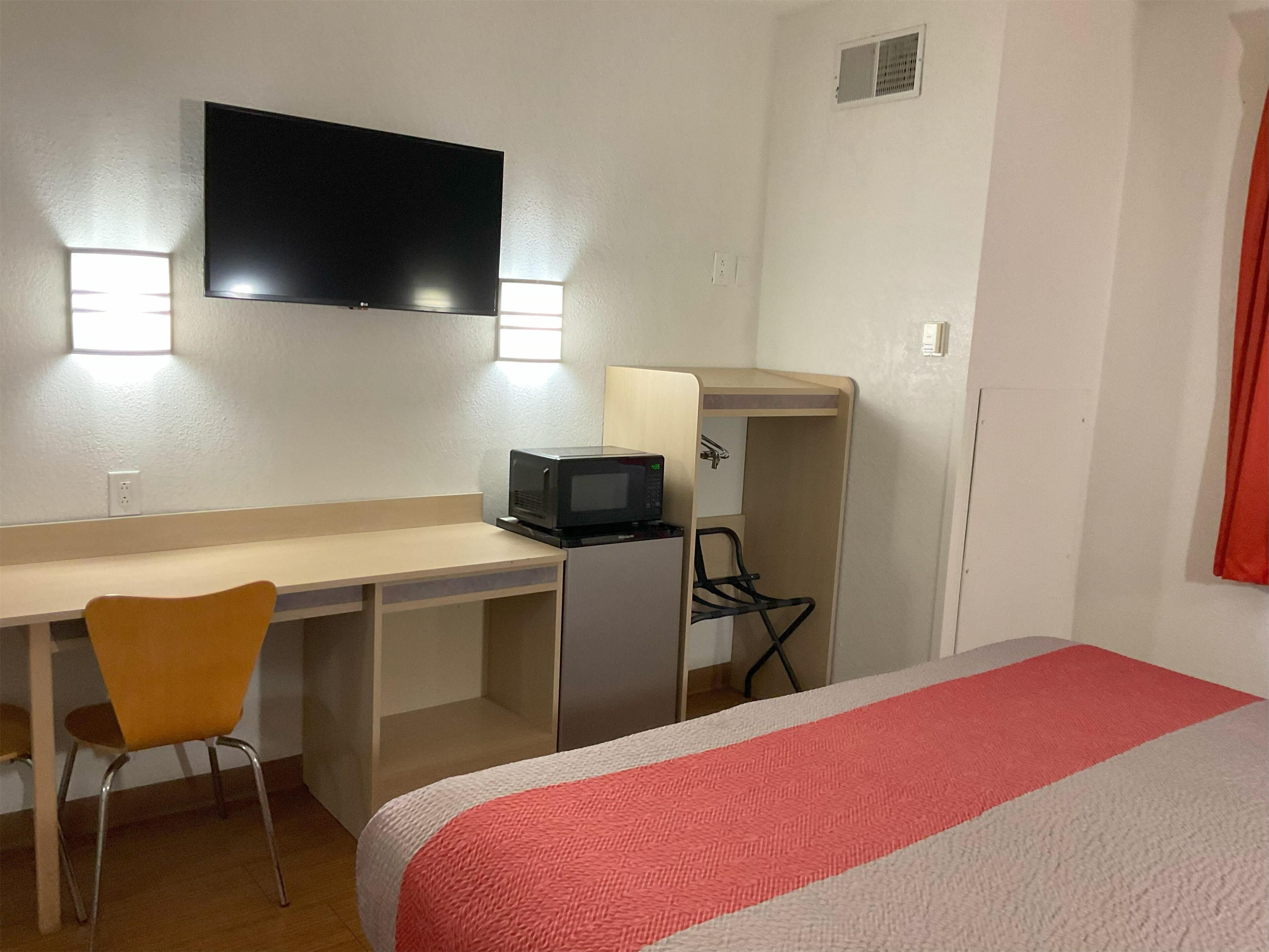 A hotel room with a bed, a desk with a chair, a television, and a microwave.