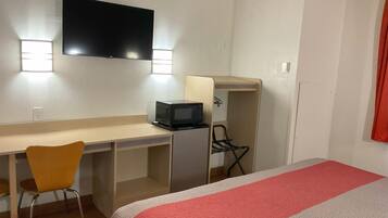 A hotel room with a bed, a desk with a chair, a television, and a microwave.