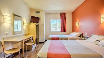 A hotel room with two beds, a desk, a chair, a TV, and a window with curtains.