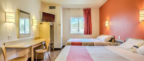 A hotel room with two beds, a desk, a chair, a TV, and a window with curtains.