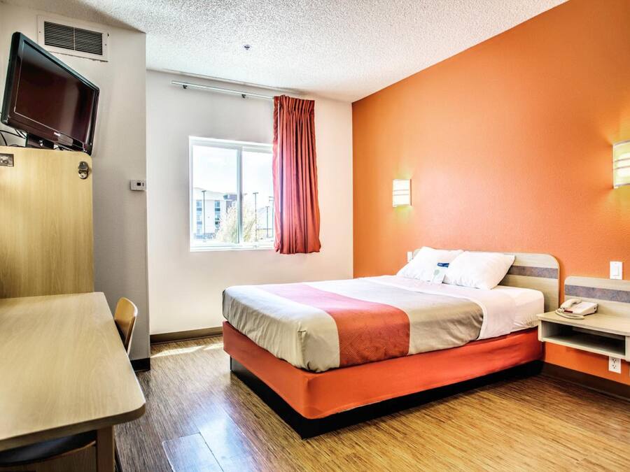 A hotel room with a bed, a desk, a television, a window with curtains, and a city view.