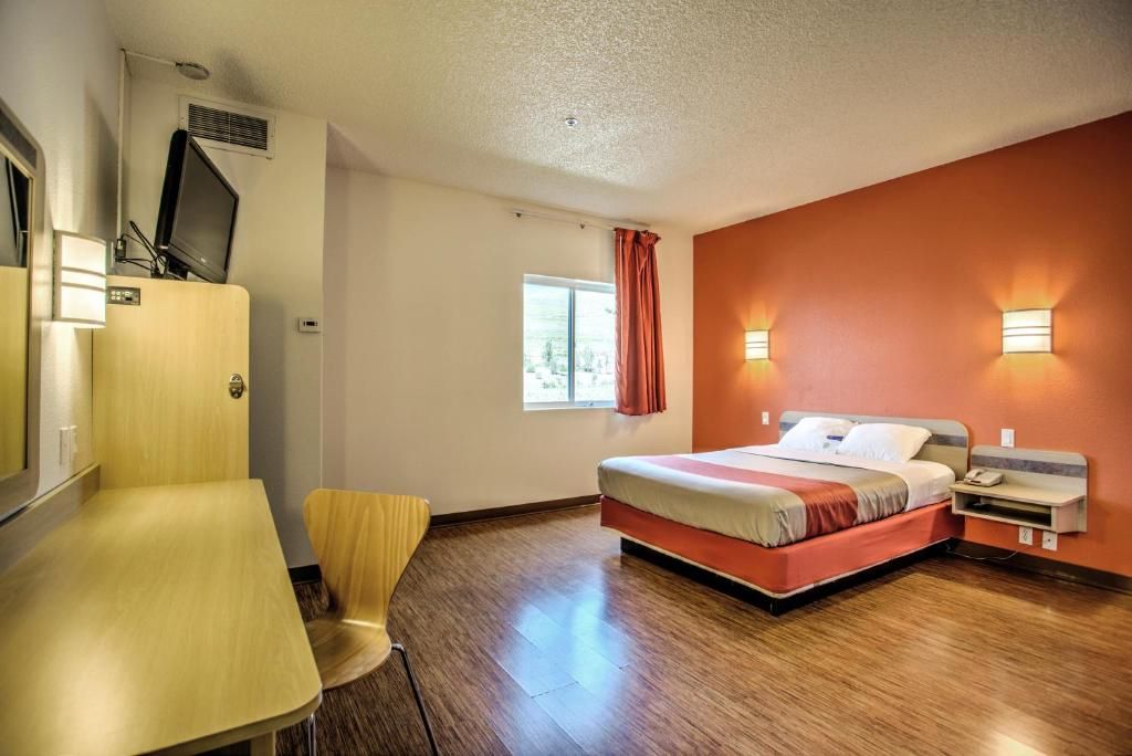 A hotel room with a bed, a desk, a chair, a television, and a window with curtains.