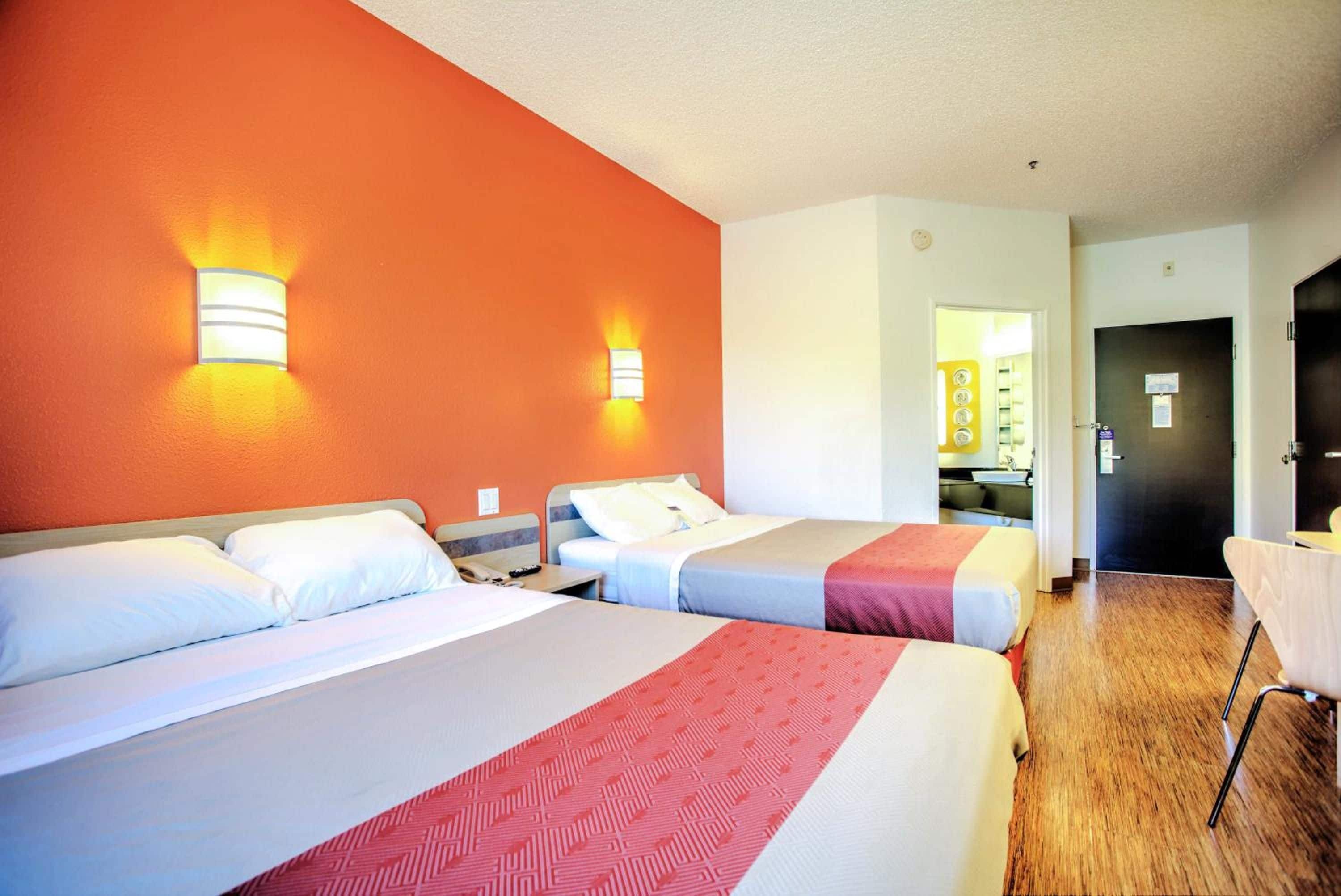 A hotel room with two beds, a wooden floor, and a bathroom visible through an open door.