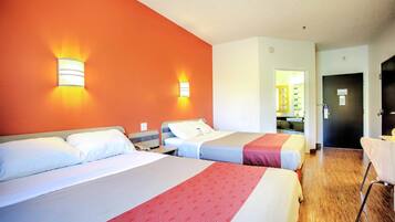 A hotel room with two beds, a wooden floor, and a bathroom visible through an open door.