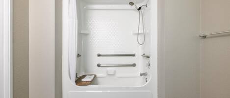Une baignoire blanche équipée d’un pommeau de douche, de barres d’appui et d’un porte-savon.