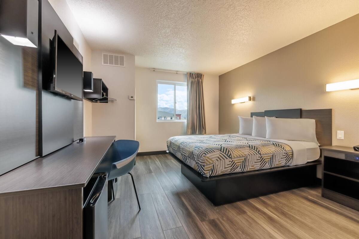 A modern hotel room with a bed, a desk, a chair, and a TV.