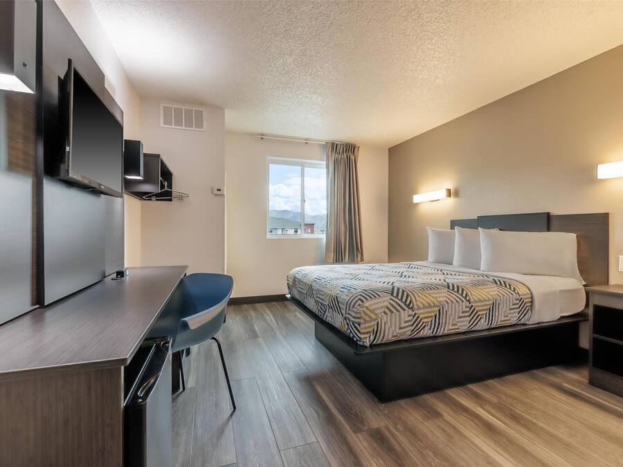 A modern hotel room with a bed, a desk, a chair, and a TV.