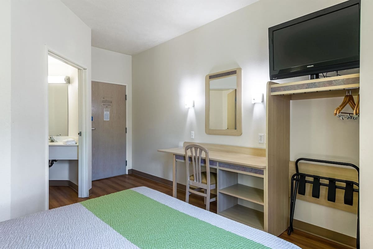 Een hotelkamer met een bed, een bureau, een stoel, een televisie en een kledingkast.