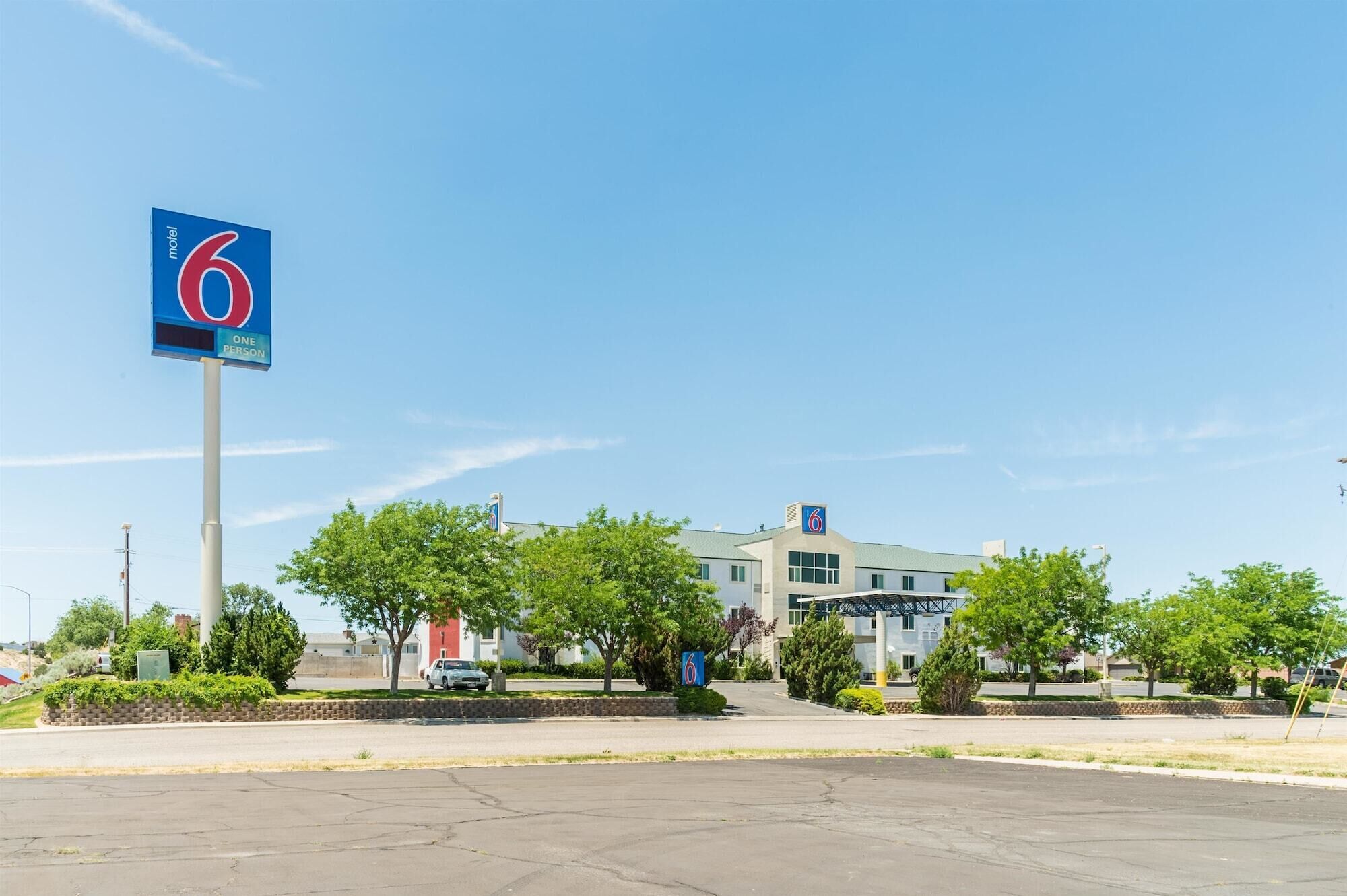A 6 Motel with a clear blue sky, a parking lot, and a building with a '6' sign on the roof.