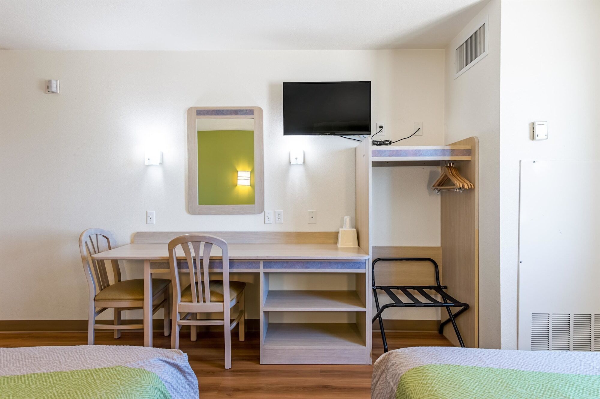 A compact room with a bed, a desk, two chairs, a TV, and a coat rack.