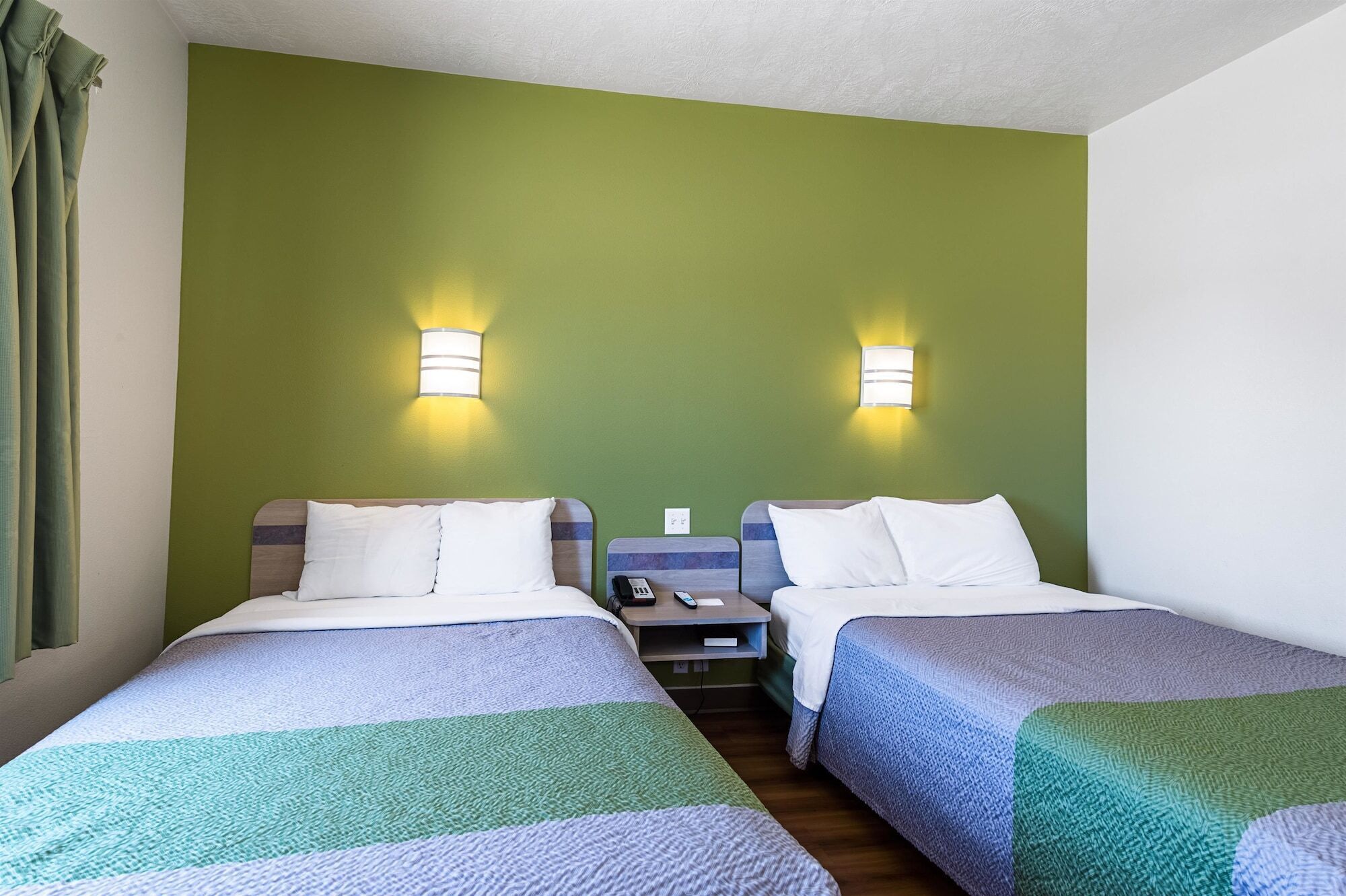 A hotel room with two beds, green walls, and two wall-mounted lights.