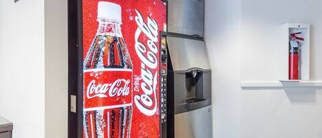 A vending machine with a Coca-Cola logo, a refrigerator, and a fire extinguisher on a wall.