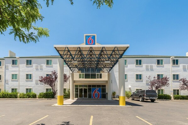 Un motel avec un grand panneau indiquant le chiffre « 6 », une entrée abritée et un parking.