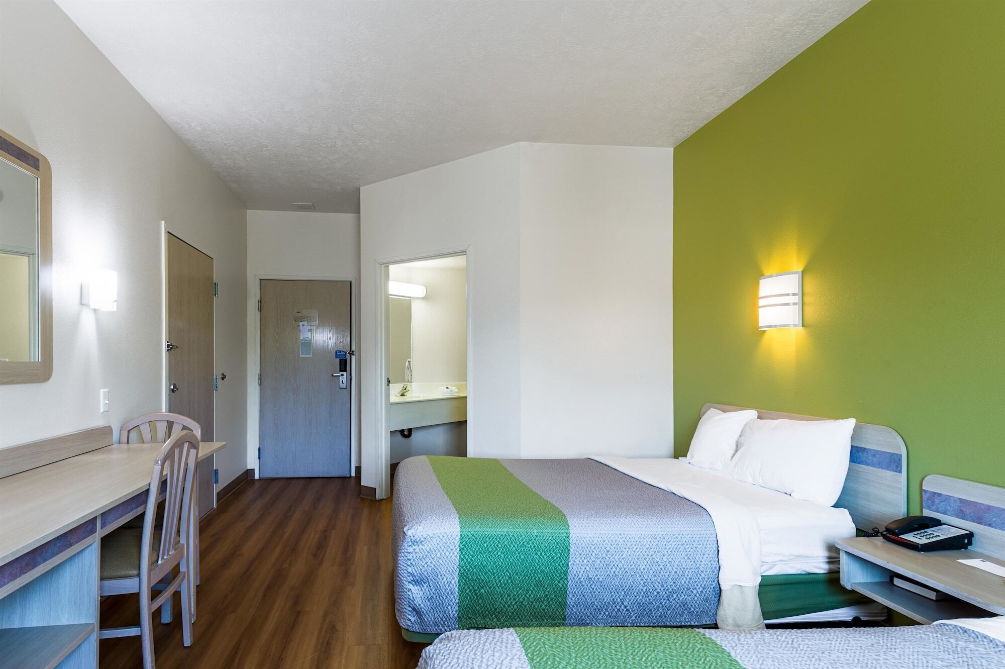Ein Hotelzimmer mit Bett, Schreibtisch, Stuhl, Spiegel und Nachttisch.