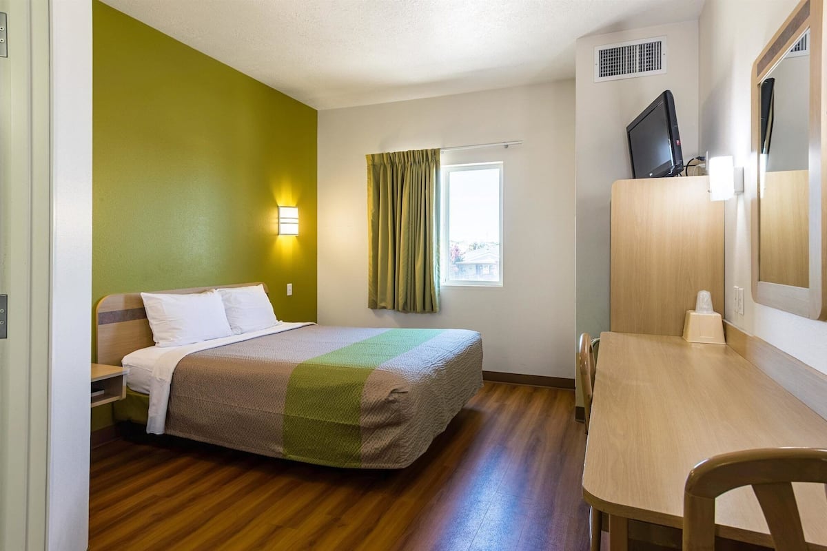 Een hotelkamer met een bed, een bureau, een stoel, een televisie en een raam met gordijnen.