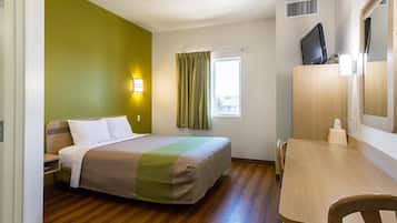 Une chambre d’hôtel équipée d’un lit, d’un bureau, d’une chaise, d’une télévision et d’une fenêtre avec des rideaux.