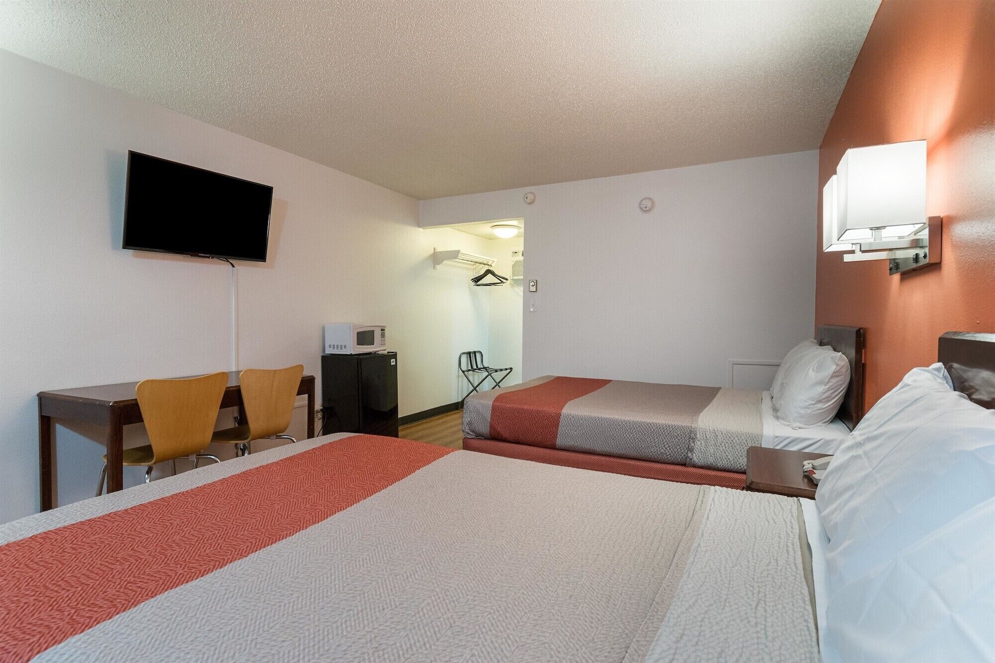 A hotel room with two beds, a desk, a chair, a TV, a microwave, and a small kitchenette.