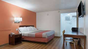 A hotel room with a bed, bedside table, chair, and a TV mounted on the wall.