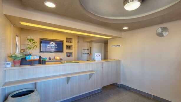 A reception desk with a digital screen displaying the hotel name, a clock, and a sign indicating check-out times. - Americas Best Value Inn Amarillo Airport (Amarillo)