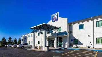 A modern building with a prominent '6' sign, a covered entrance, and a parking lot with several cars.
