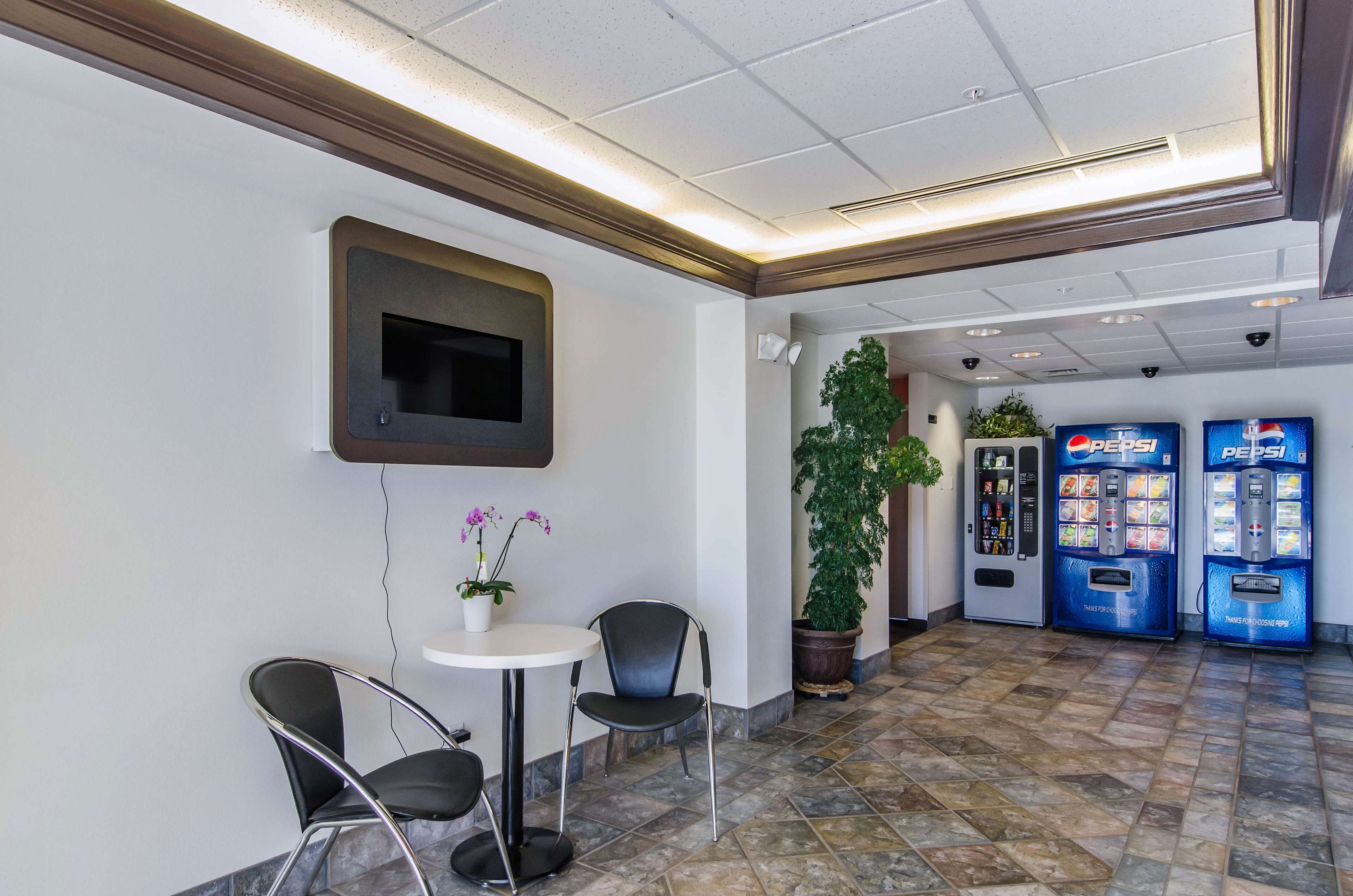 A lobby with a seating area, a television mounted on the wall, a potted plant, and two Pepsi vending machines.