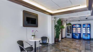 A lobby with a seating area, a television mounted on the wall, a potted plant, and two Pepsi vending machines.