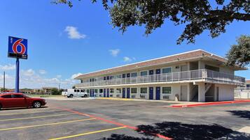 A motel with a blue sign, a parking lot, and a building with multiple rooms.