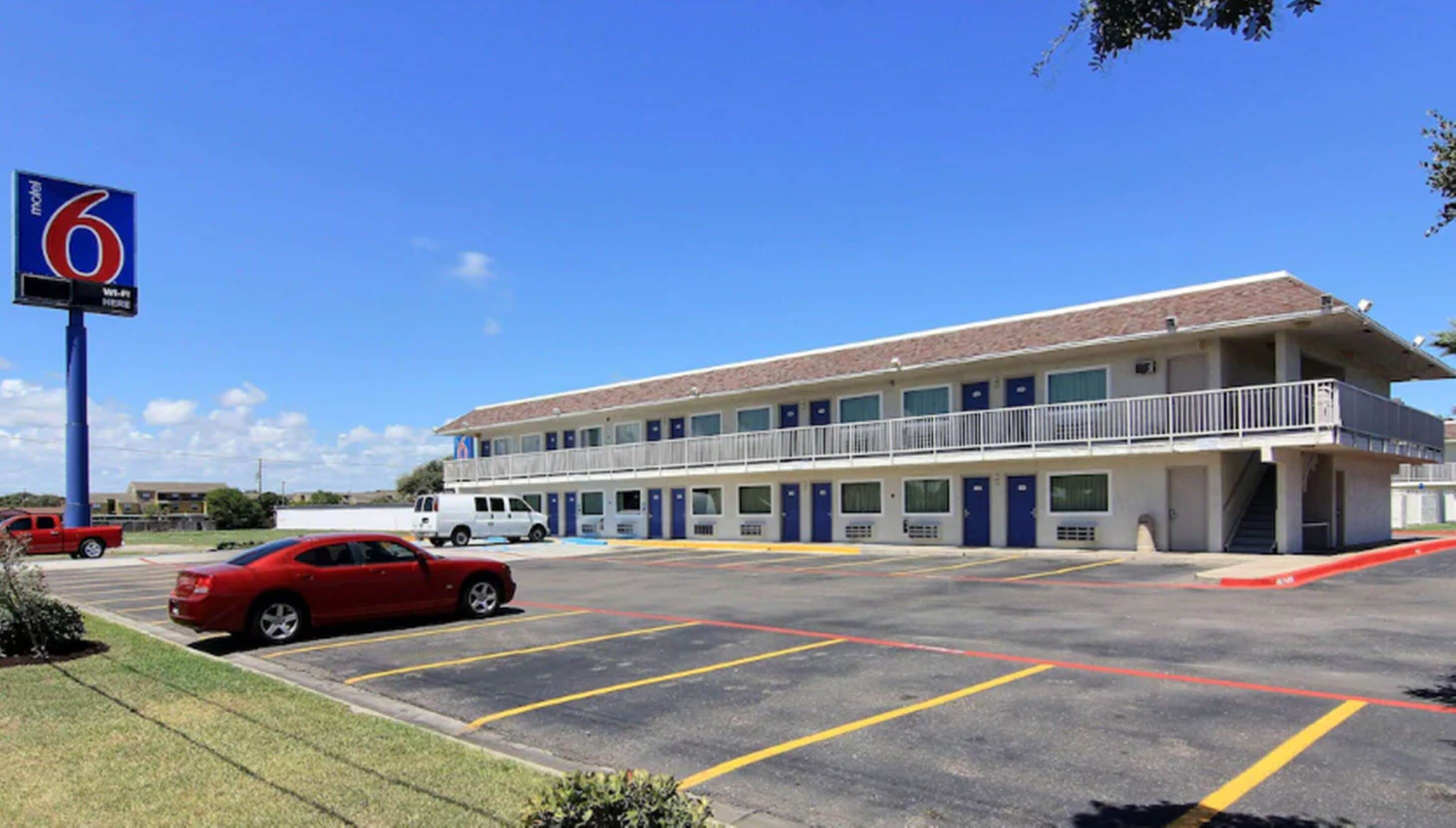 A motel with a two-story building, a parking lot, and a red car parked in the lot.