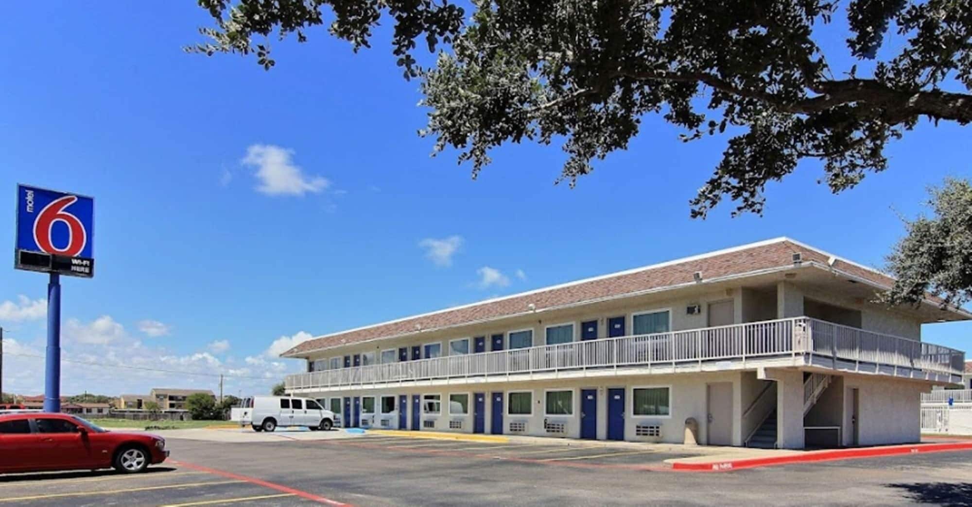 A motel with a two-story building, a parking lot, and a red car parked in front.