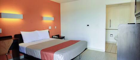 A modern hotel room with a bed, bedside tables, a chair, and a bathroom visible through an open door.