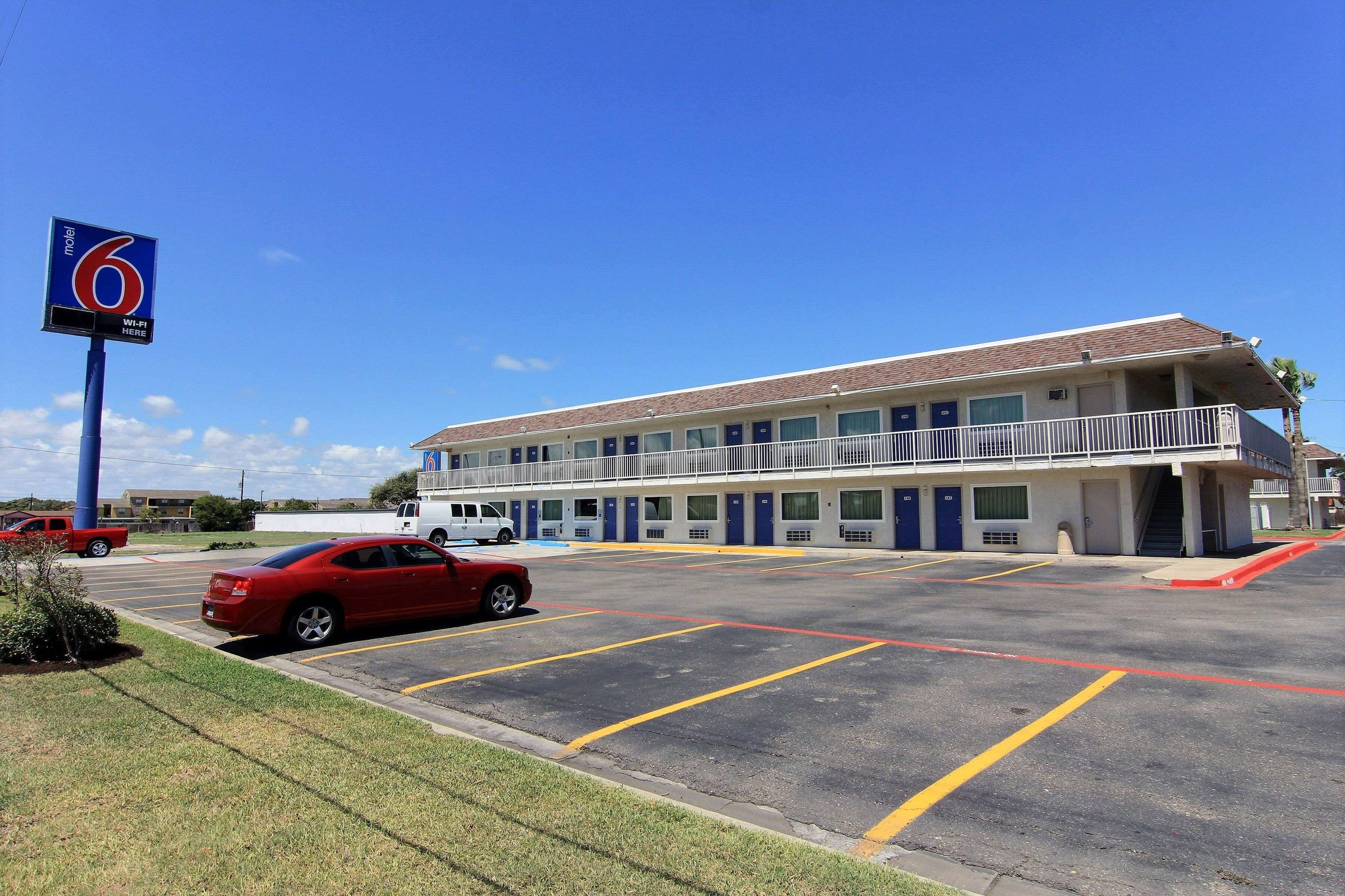 A motel with a large parking lot, a red car parked in the lot, and a sign indicating the motel's name.