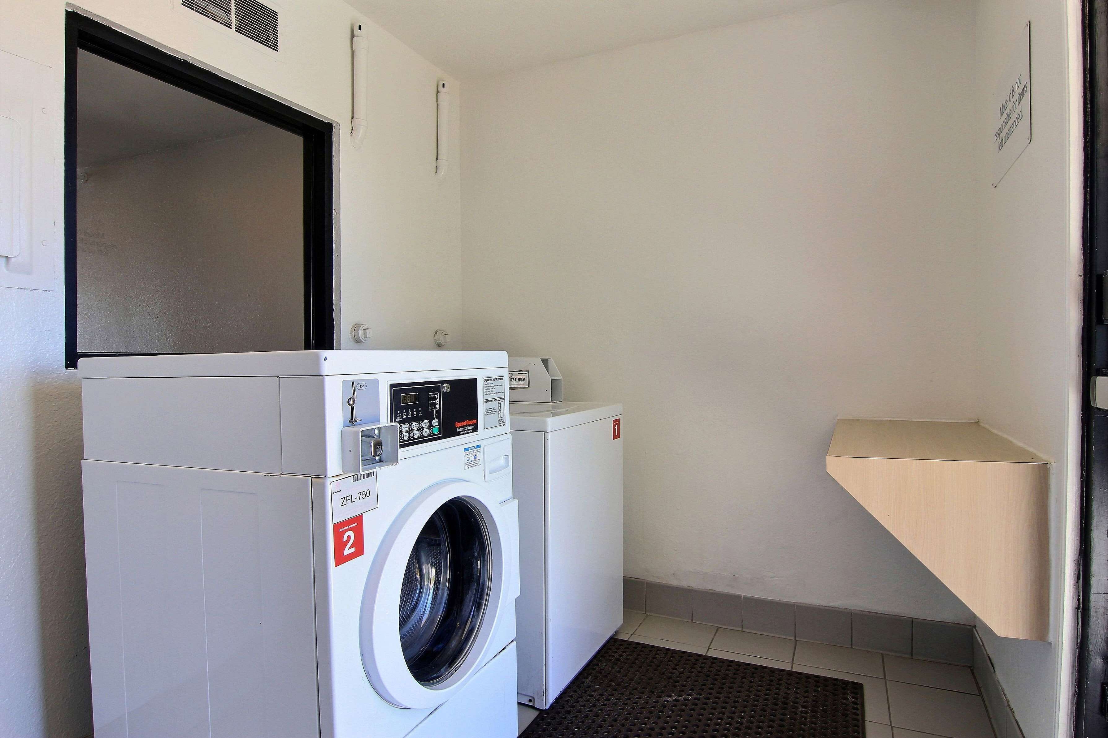 A laundry room with two white washing machines, a vent on the wall, and a small shelf.