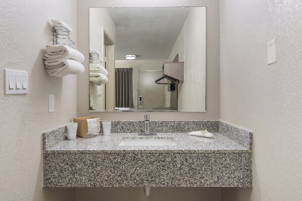 Un baño con encimera de granito, un lavabo, un espejo y toallas colgadas en un perchero.