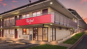 Red Roof Inn -hotelli, jossa on kaksikerroksinen rakennus, parveke ylemmässä kerroksessa ja pysäköintialue edessä.