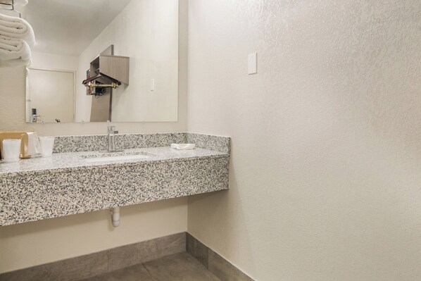 A bathroom with a granite countertop, a sink, a mirror, and a towel rack. - Red Roof Inn Fort Worth South (Fort Worth)